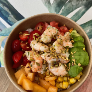 IMG_09601 copie - AMOHI Poke bowl with shrimp, avocado, cherry tomatoes, corn, and melon, topped with chopped pistachios over rice in a brown bowl.