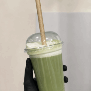 matcha classic - AMOHI Gloved hand holding a green smoothie in a clear cup with a dome lid and a large brown straw.