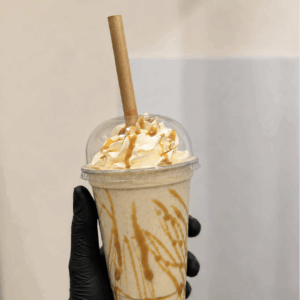 milkshake - AMOHI Hand wearing a black glove holds a caramel drizzle milkshake with whipped cream in a clear cup and a wafer stick on top.